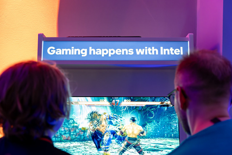 Two gamers playing on an Intel branded arcade machine with the words Gaming happens with Intel on the top of the machine